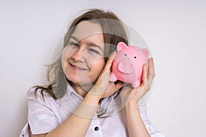 Young woman is holding piggy money bank in hands and dreaming