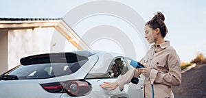 Young woman holding power supply cable from her electric car, prepared for charging it in home, sustainable and economic