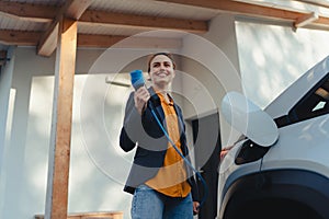 Young woman holding power supply cable from her electric car, prepared for charging it in home, sustainable and economic