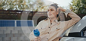 Young woman holding power supply cable from her electric car, prepared for charging it in home, sustainable and economic