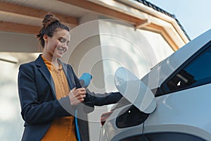 Young woman holding power supply cable from her electric car, prepared for charging it in home, sustainable and economic