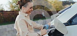 Young woman holding power supply cable from her electric car, prepared for charging it in home, sustainable and economic