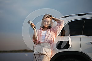 Young woman holding power supply cable from her electric car, prepared for charging it sustainable and economic