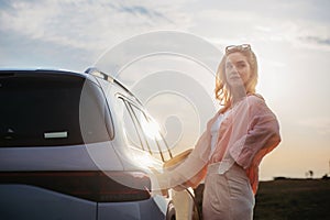 Young woman holding power supply cable from her electric car, prepared for charging it sustainable and economic