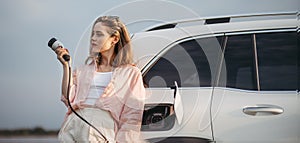 Young woman holding power supply cable from her electric car, prepared for charging it sustainable and economic