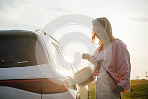 Young woman holding power supply cable from her electric car, prepared for charging it sustainable and economic