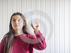 Young woman holding a question mark sign with confused and doubt expression.