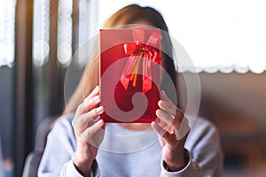 A young woman holding a red present box cover her face