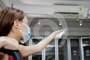 Young woman holding remote control of air conditioner
