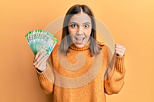 Young woman holding russian 200 ruble banknotes pointing thumb up to the side smiling happy with open mouth