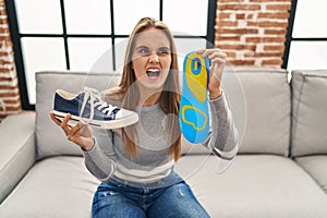 Young woman holding shoe insole angry and mad screaming frustrated and furious, shouting with anger