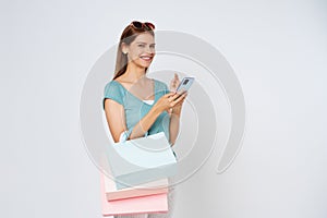 Young woman holding shopping bags while using mobile phone isolated over white background