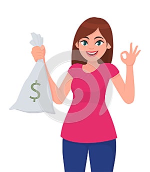 Young woman holding/showing cash, money, currency note bag with dollar sign and gesturing or making okay/OK sign with hand fingers