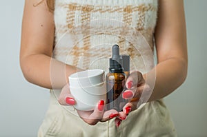 Young woman holding and showing with her hands set of skin care products, serum, creams, personal beauty care concept