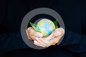 Young woman holding small planet in hands against black background. Ecology, environment and Earth day concept.