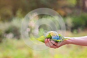 Young woman holding small planet in hands against spring or summer green background with copy space. Ecology