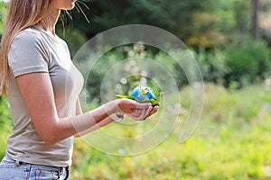 Young woman holding small planet in hands against spring or summer green background. Ecology, environment and Earth day