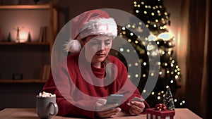 Young woman holding a smartphone phone and credit card in decorated christmas home room. Online holiday shopping