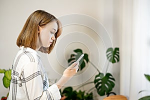 Young woman holding smartphone using mobile apps, chatting in social media at home in cozy living room.
