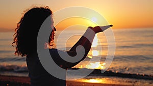 Young woman holding sun on hands, meditating near the sea