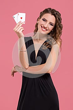 Young woman holding two aces in hand against on pink background