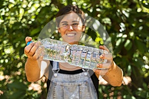 A young woman holding up a plastic bottle refilled with clear natural spring water.