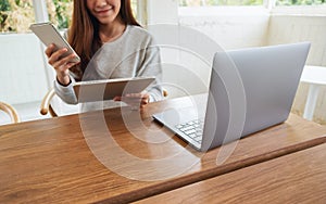 A woman holding and using mobile  phone , tablet pc and laptop computer on wooden table