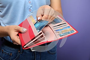 Young woman holding wallet with credit cards on color background, closeup