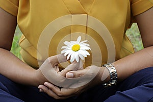 Young woman holding a white daisy flower in hand, cross-legged in yoga or prayer pose gesture. Be balance, find balance in life.