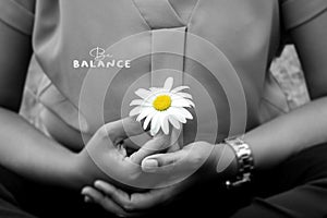 Young woman holding a white daisy flower in hands, cross-legged in yoga or prayer pose gesture. Be balance concept.