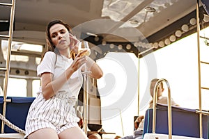 Young woman holding a wineglass and sitting on deck of sailing yacht