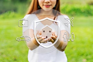 Young woman holding wooden house model with car, family, travel and health insurance icons and concept