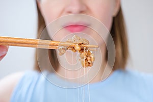 Young woman holding wooden sticks with Japanese fermented natto beans front view close-up, selective focus.