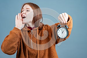 a young woman holds an alarm clock in one hand, the other hand is put to her mouth to hear better