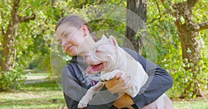 Young woman holds in arms white playful doggy in autumn park