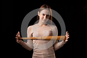 A young woman holds a bat in her hands and calmly looks into the camera. Black background. Self-defense, psychological protection