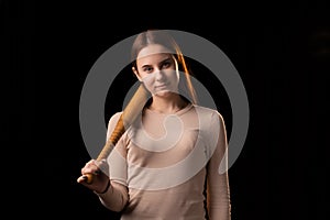 A young woman holds a bat in her hands and calmly looks into the camera. Black background. Self-defense, psychological protection