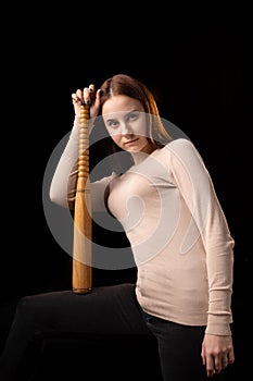 A young woman holds a bat in her hands and calmly looks into the camera. Black background. Self-defense, psychological protection