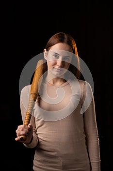 A young woman holds a bat in her hands and calmly looks into the camera. Black background. Self-defense, psychological protection