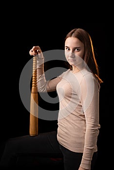 A young woman holds a bat in her hands and calmly looks into the camera. Black background. Self-defense, psychological protection