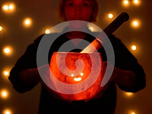 Young woman holds a comically carved Halloween pumpkin with a cute face, illuminated by a burning candle inside