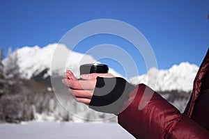 A young woman holds a cup of tea against the background of mountains in winter. Strbske Pleso Lake, Slovakia