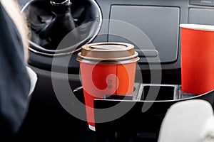 Young woman holds disposable cup of coffee in the car, to keep concentrated while driving