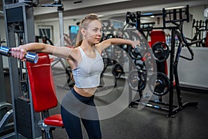 Young woman holds dumbbells in her hands and works out in the gym performing an exercise