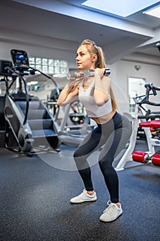 Young woman holds dumbbells in her hands and works out in the gym performing an exercise