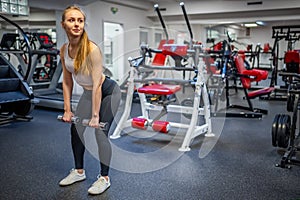 Young woman holds dumbbells in her hands and works out in the gym performing an exercise