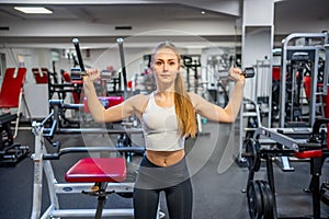 Young woman holds dumbbells in her hands and works out in the gym performing an exercise