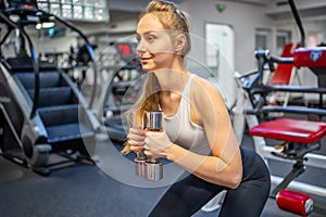 Young woman holds dumbbells in her hands and works out in the gym performing an exercise