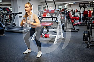 Young woman holds dumbbells in her hands and works out in the gym performing an exercise