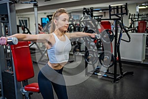 Young woman holds dumbbells in her hands and works out in the gym performing an exercise